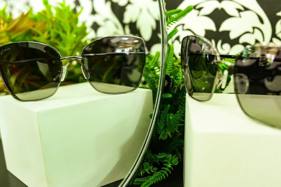 Óculos de sol com armação de metal e proteção UV expostos entre plantas na Óptica Visualisi, Porto Alegre