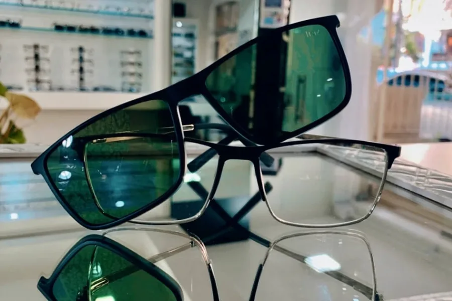 Óculos de sol com lentes verdes e armação retangular sobre a vitrine da Óptica Visualisi, Porto Alegre